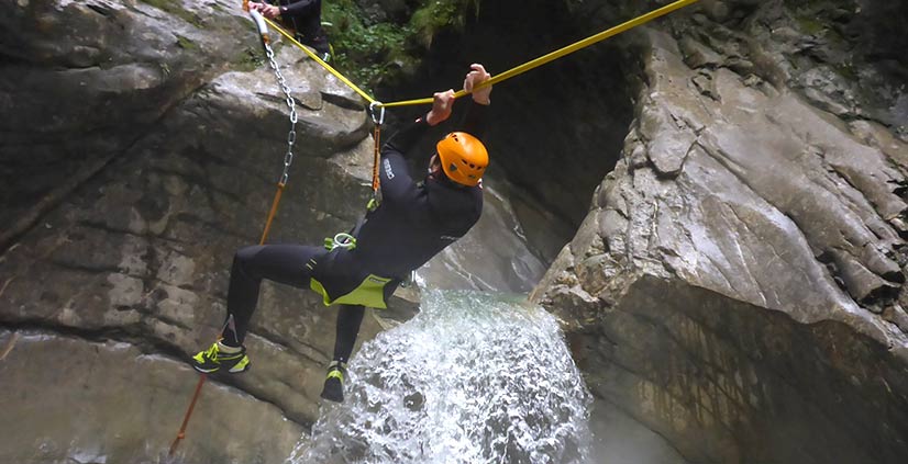Ein Mann beim Canyoning, der mit Seil Hindernisse überwindet